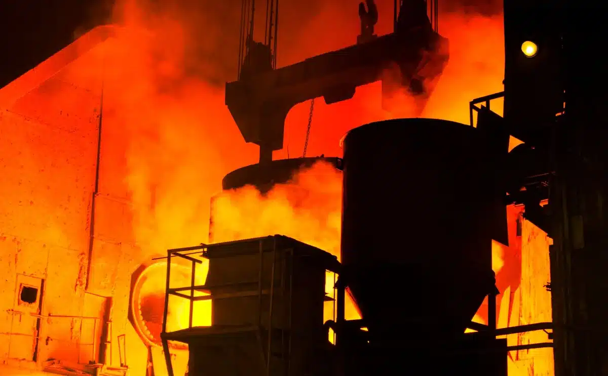 Operai in cantiere presso impianto siderurgico con bobine d'acciaio e macchinari industriali