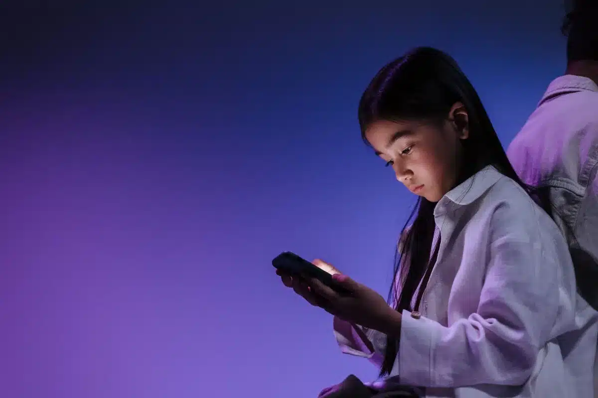 Adolescente con smartphone illuminato in primo piano, simbolo della dipendenza dai social media
