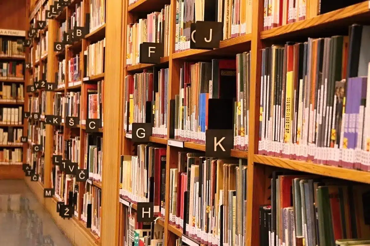 Lettore seduto a una scrivania circondata da libri aperti, illuminato da una lampada calda