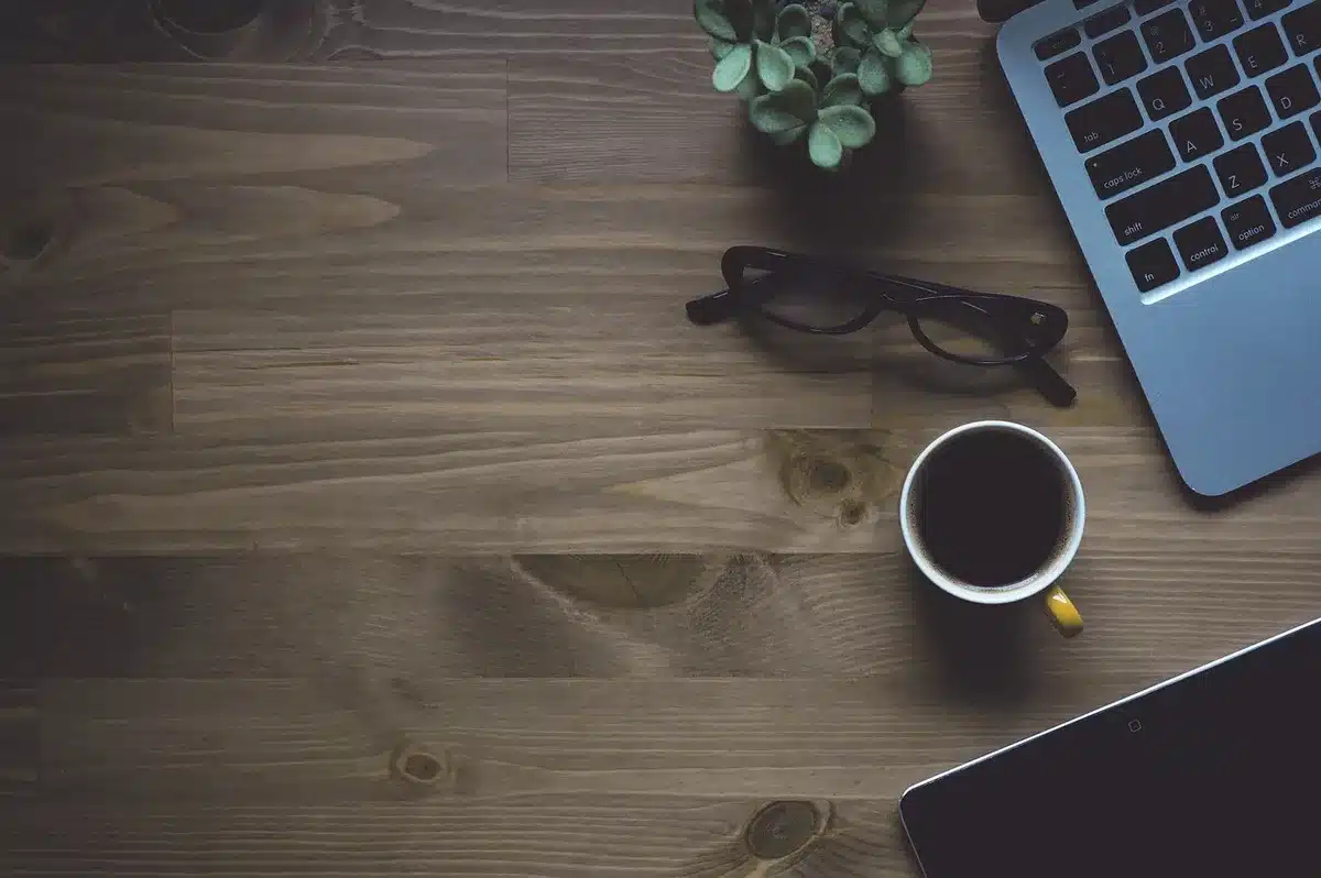 Scrivania condivisa con laptop, tazza di caffè e bloc-notes in un ufficio moderno
